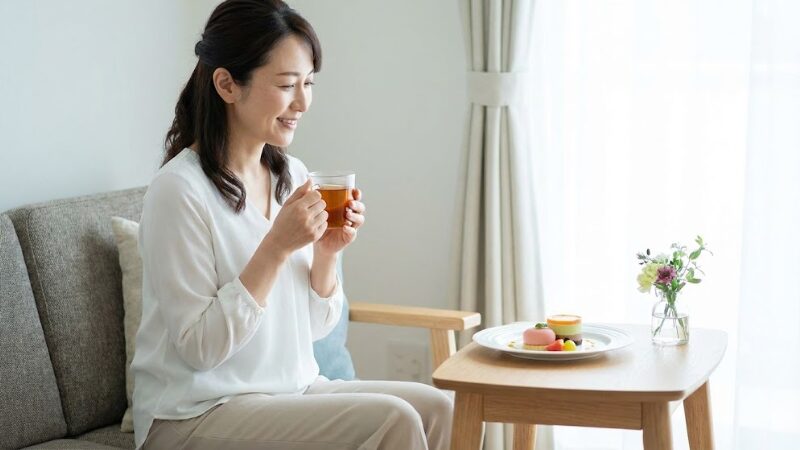 ５０代女性の介護者が飲み物を飲みながらゆっくりくつろいでいる様子。「がんばりすぎない」ことを表している。