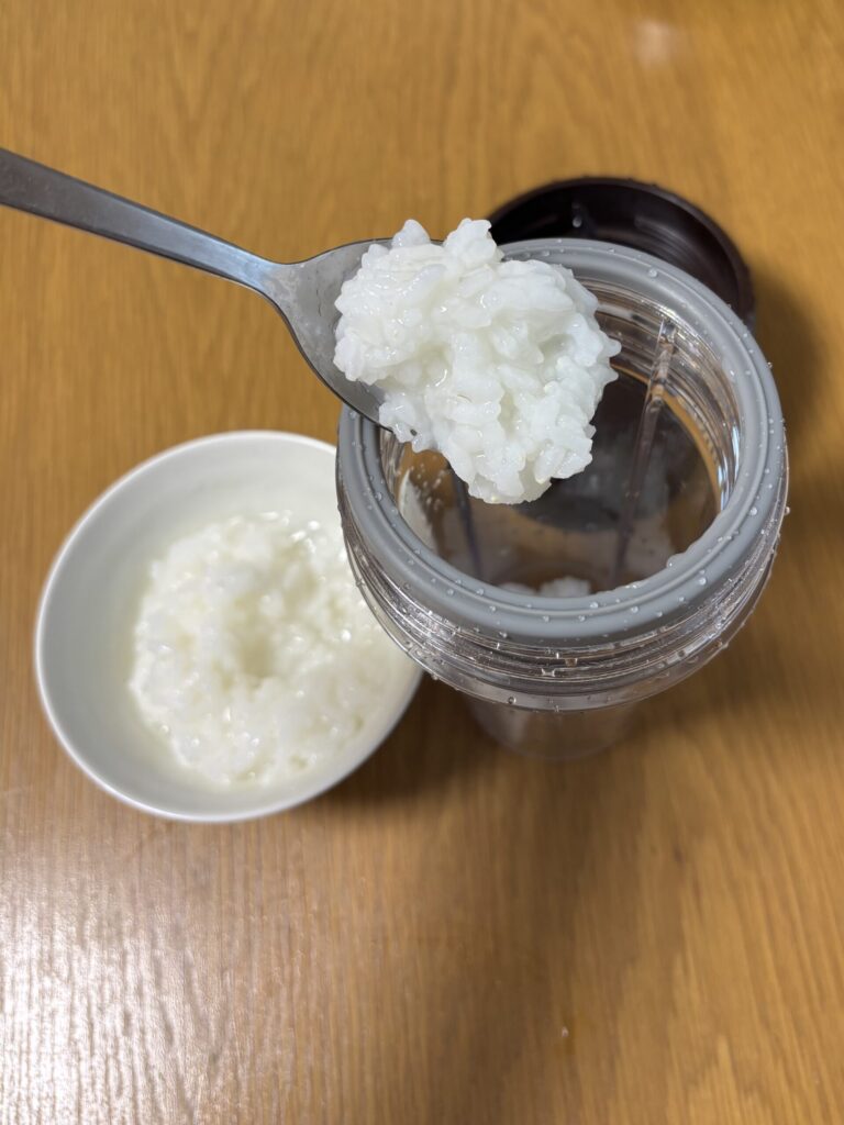 お粥をスプーンでミキサー容器に入れている所