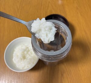 お粥をスプーンでミキサー容器に入れている所
