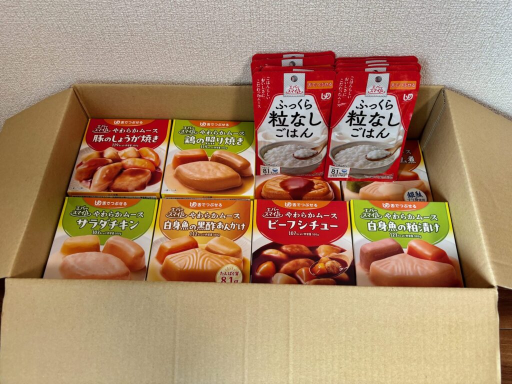 エバースマイルのやわらかムース食(主菜30品)とふっくら粒なしごはん10袋が段ボールに入っている写真