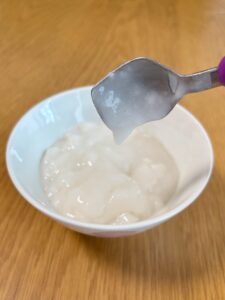 キユーピー「なめらかごはん」をのせたスプーンを傾けた写真。スプーンにほとんど残らず、のどへの張り付きが少ないことがわかる。
