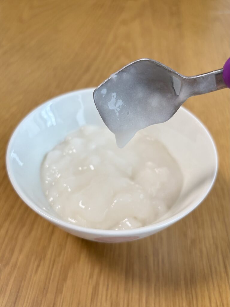 キユーピー「なめらかごはん」をのせたスプーンを傾けた写真。スプーンにほとんど残らず、のどへの張り付きが少ないことがわかる。
