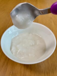 キユーピー「なめらかごはん」をレンジで温めたあと。スプーンですくい、傾けて、粥が落ちる様子を確認している写真。