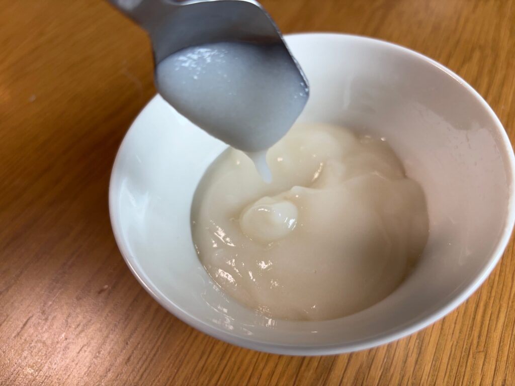 ミキサーにかけたごはんをスプーンですくい、ぽってりと垂らしてとろみの状態を確認している様子
