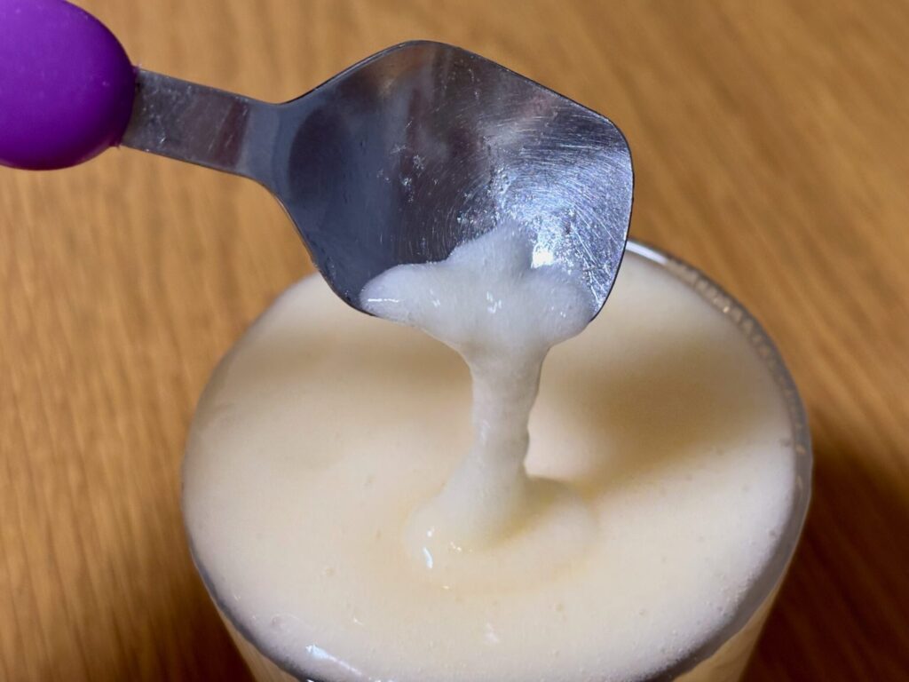 ミキサーゲル1gで作ったオレンジジュースのムース食をスプーンですくい、傾けるとサラッと流れ落ちる様子