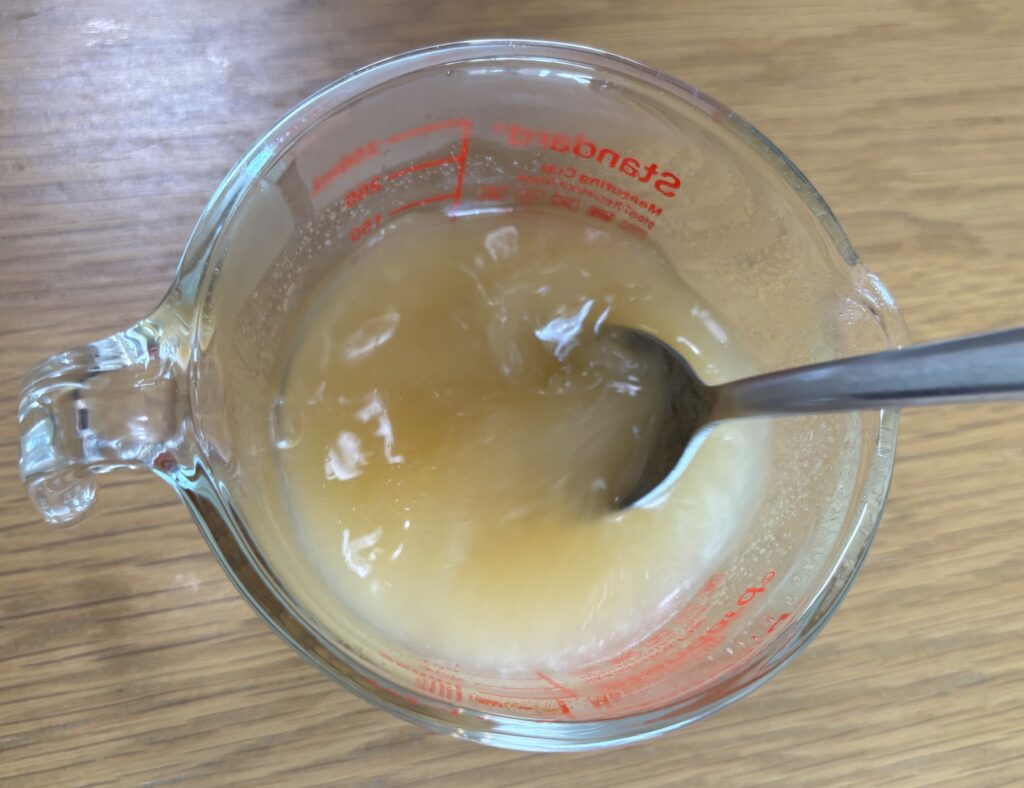 計量カップのだし汁にとろみエールを入れ、スプーンでかき混ぜているところ