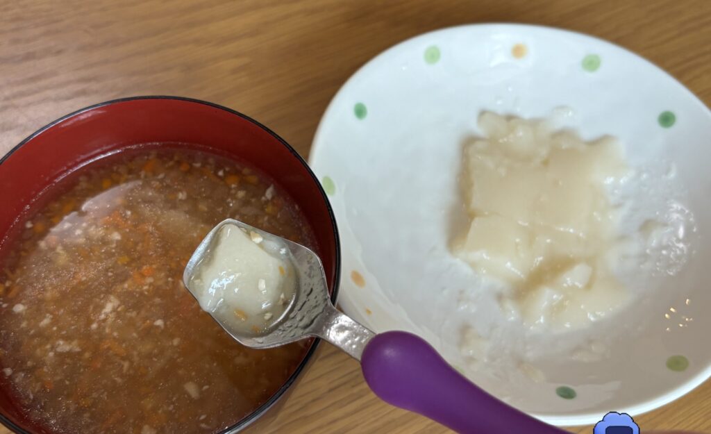 汁椀に刻みのお雑煮、別の小皿にスプーンで食べるおもちを分けて置き、スプーンで一口すくっているところ